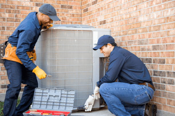 Two HVAC technicians repairing a large outdoor air conditioning system beside a brick building during a residential HVAC maintenance and repair service.