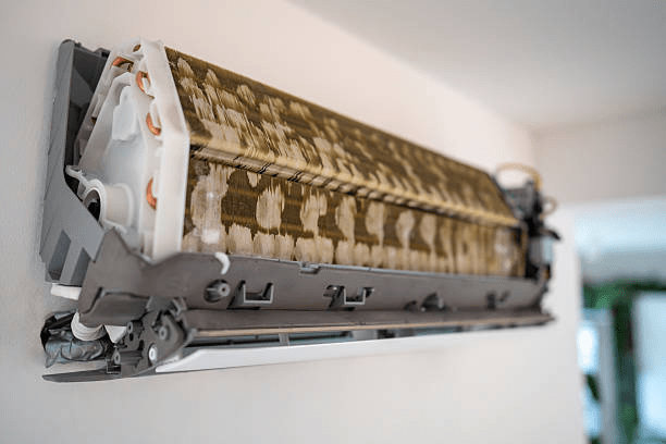 A wall-mounted split air conditioner with exposed dirty evaporator coils, showing buildup that can reduce HVAC efficiency and indoor air quality.