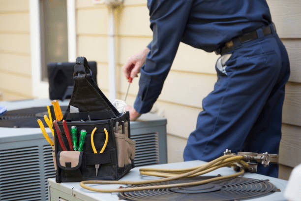 An HVAC technician servicing an outdoor air conditioning unit with professional repair tools during a residential heating and cooling maintenance visit.