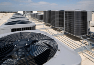 Rows of rooftop HVAC condenser units with large fans on a commercial building roof
