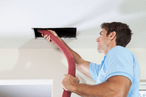 HVAC technician cleaning an indoor air duct using a flexible vacuum hose.